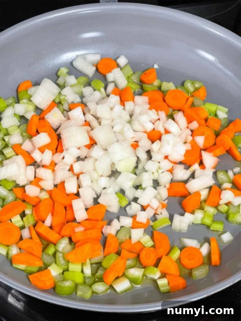 Freshly diced mirepoix vegetables (onions, celery, carrots) in a skillet before cooking.