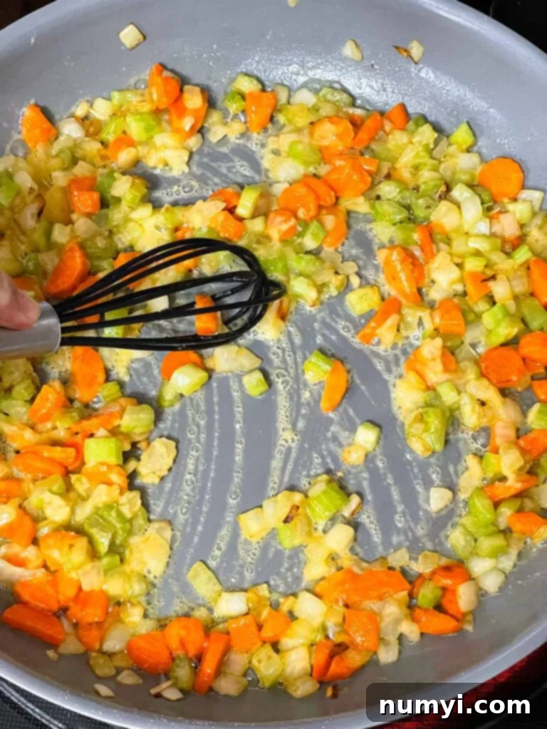 A smooth roux cooking with mirepoix in a skillet, forming the base of the creamy sauce.