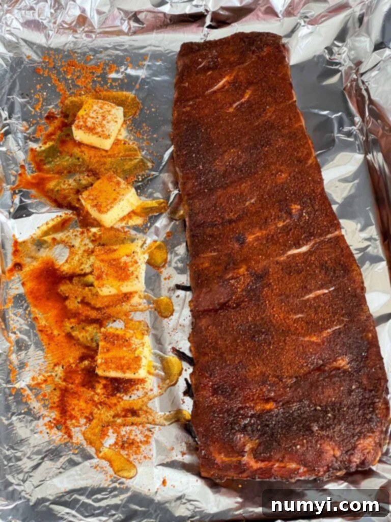 Ribs being carefully wrapped in heavy-duty aluminum foil with butter, honey, and vinegar.