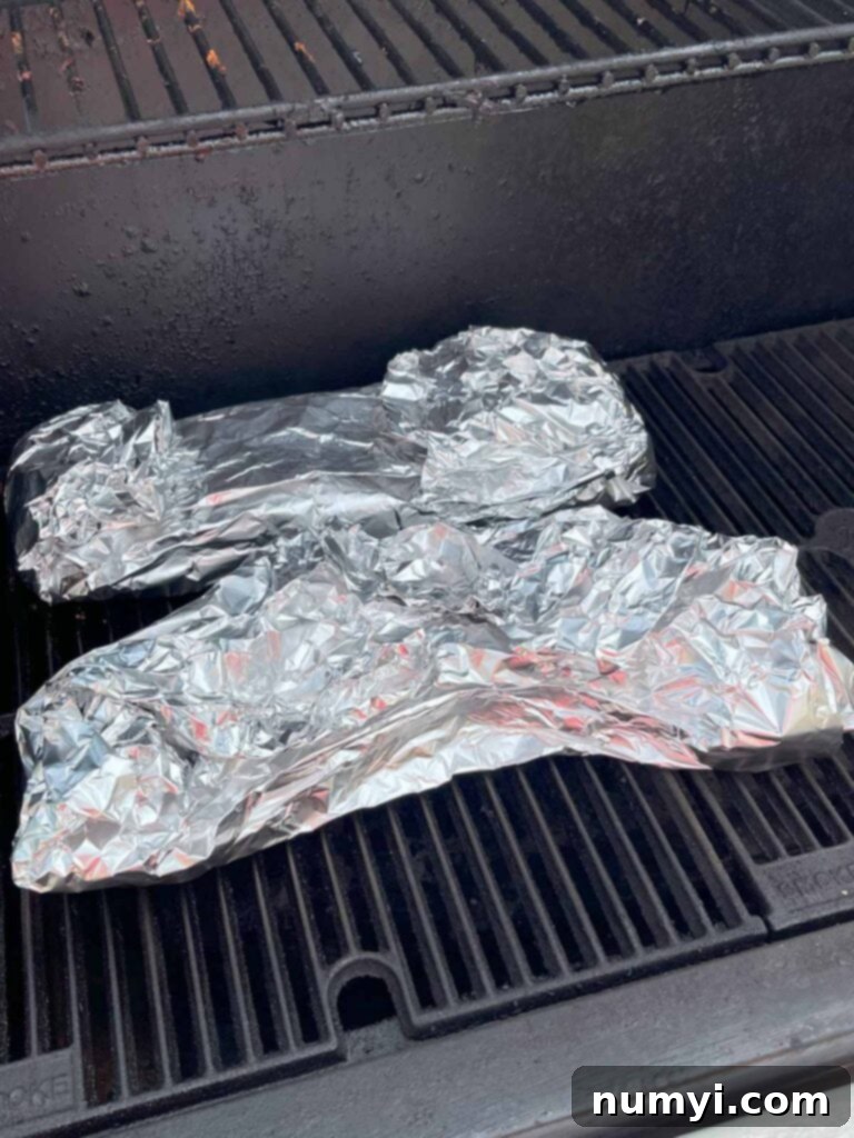 Foil-wrapped ribs placed back on the smoker grates to continue cooking.