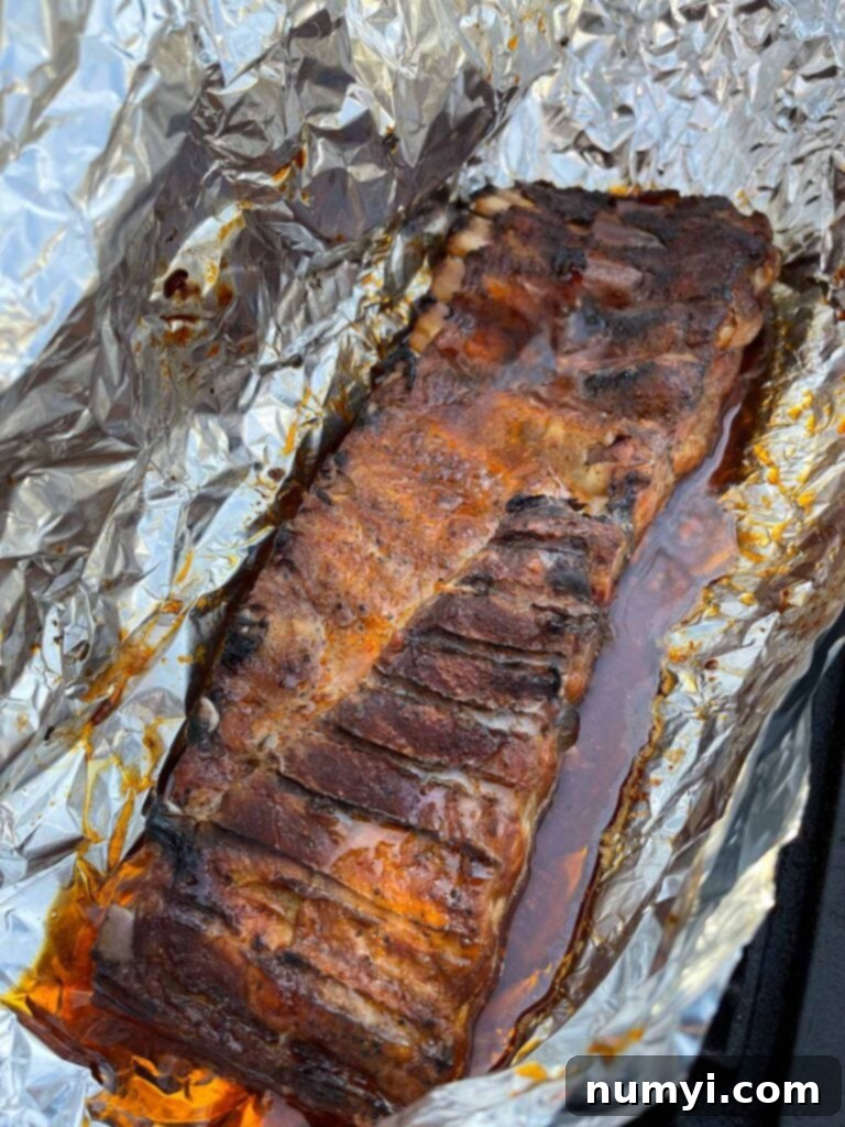 Foil-wrapped ribs just opened, revealing tender, cooked meat.