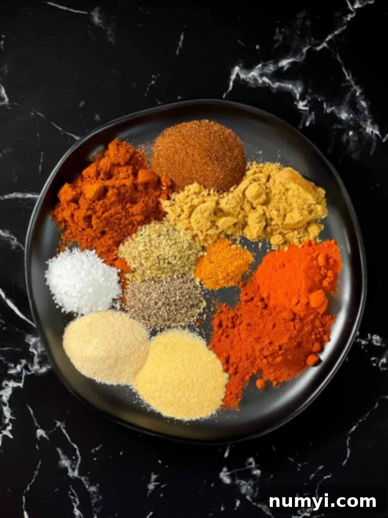 Individual spices including chili powder, cumin, paprika, and oregano arranged in small piles on a dark surface, ready for mixing.