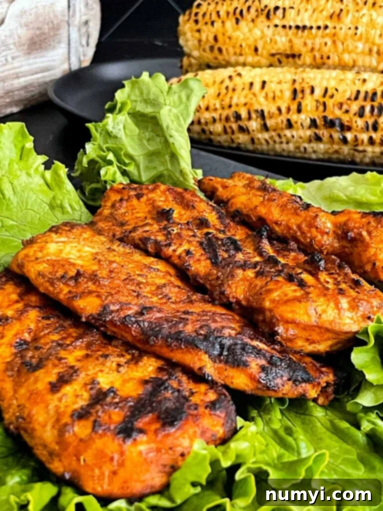 Perfectly grilled Southwest chicken breasts served on a bed of fresh greens with charred corn on the cob in the background.