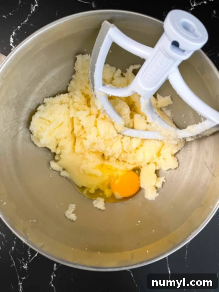 Adding eggs one by one to the butter and sugar mixture in a stand mixer.