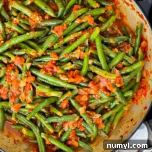 Green beans with tomato sauce in a dark bowl.