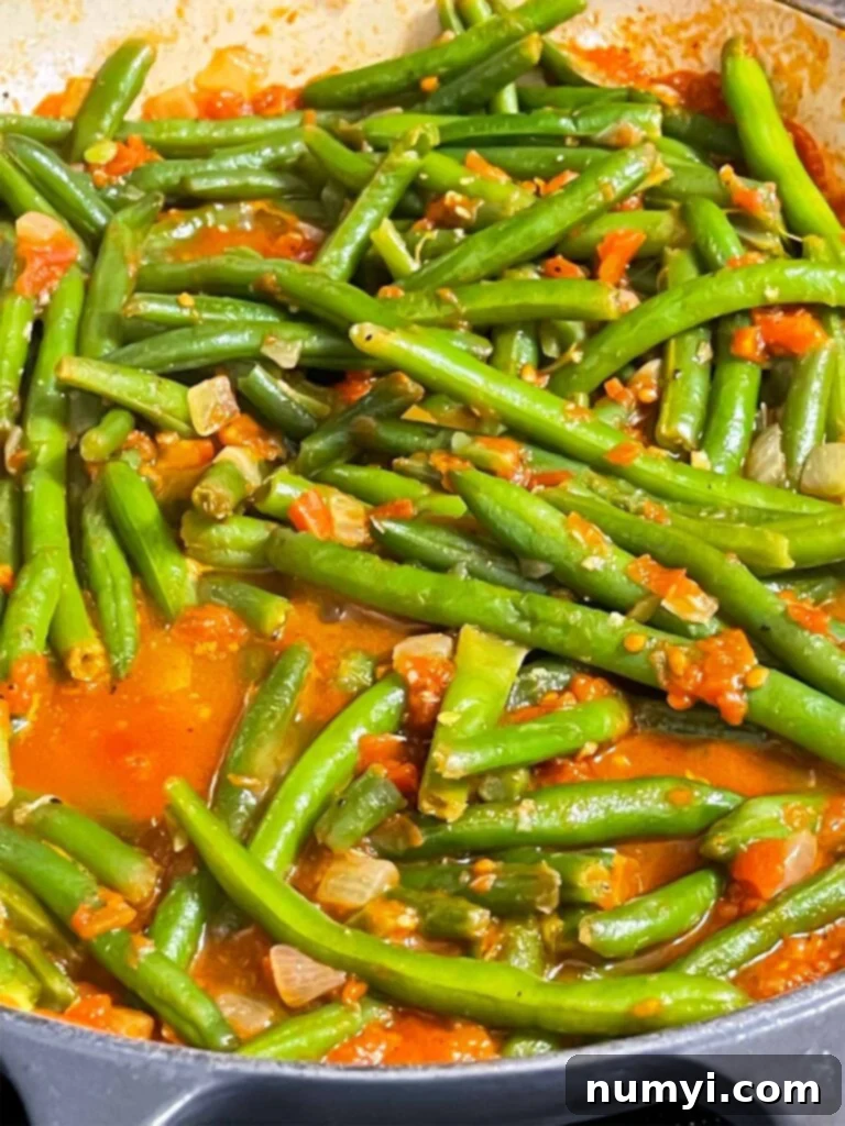 Green beans with tomato sauce cooking in a large skillet.