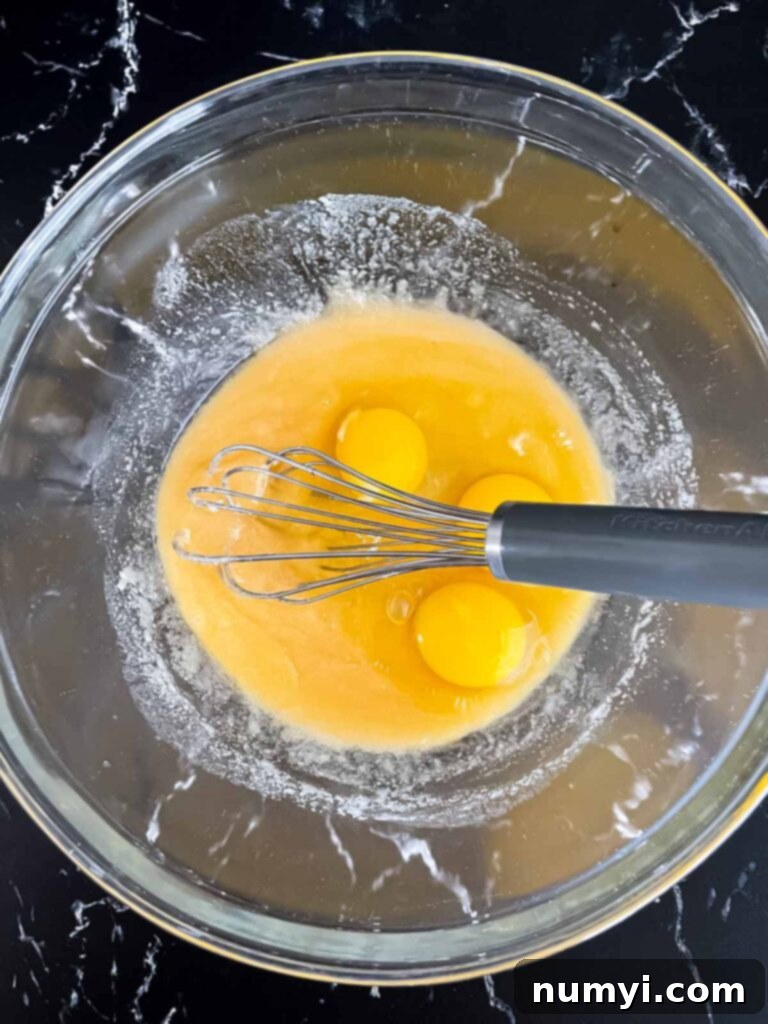 Eggs added to a sugar butter mixture in a glass bowl.