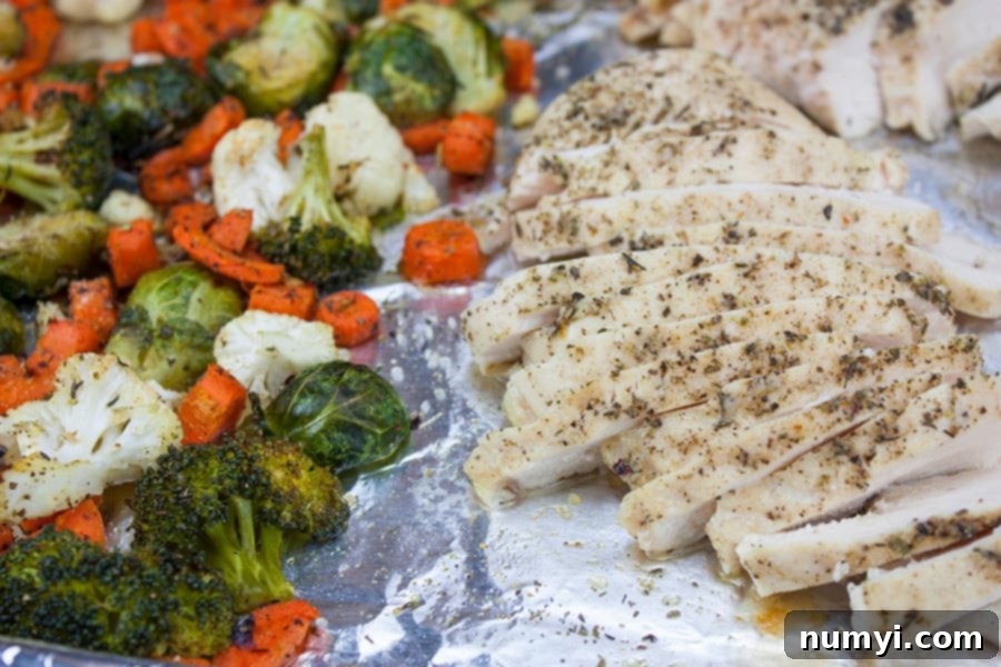 Sheet pan chicken and vegetables on a foil lined baking pan, showcasing golden roasted chicken and perfectly tender vegetables.