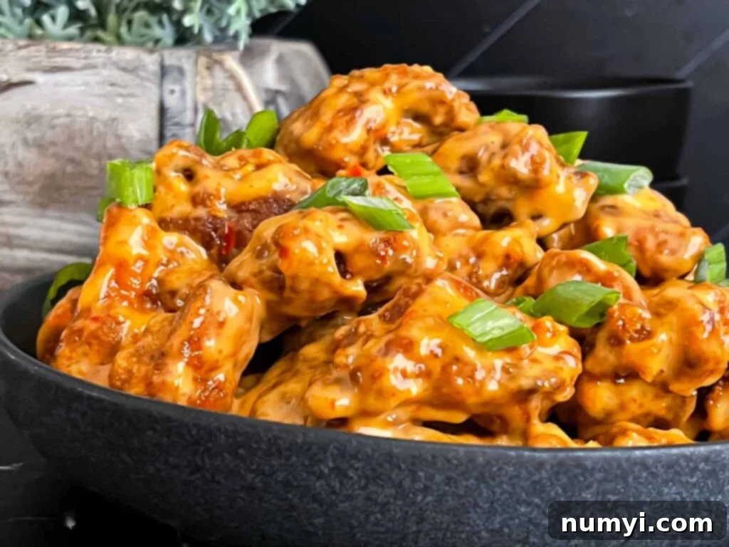 Bang Bang Chicken in a dark bowl, garnished with green onion.