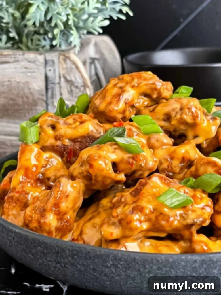 Bang Bang Chicken in a dark bowl, garnished with green onion.