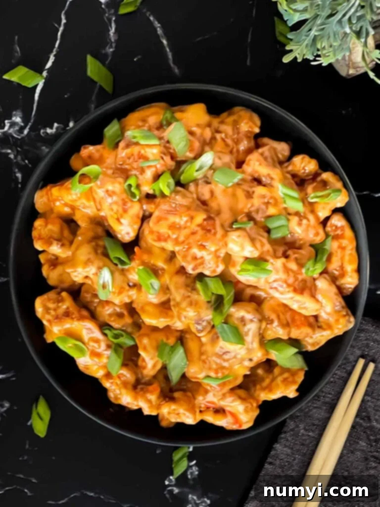 Bang Bang Chicken in a dark bowl, garnished with green onion.