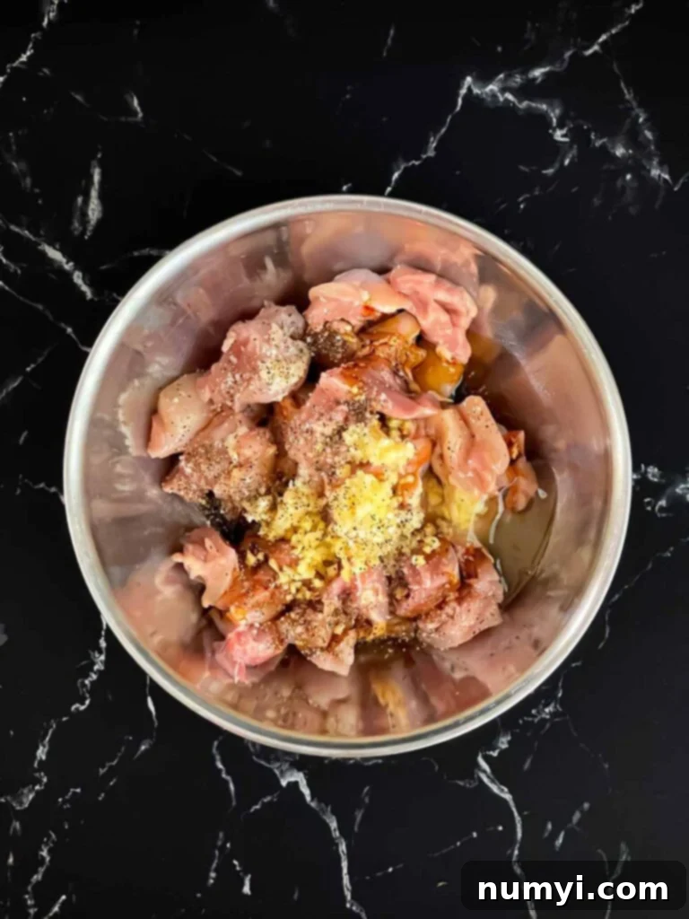 Bite sized pieces of chicken thigh in a bowl with spices on top.