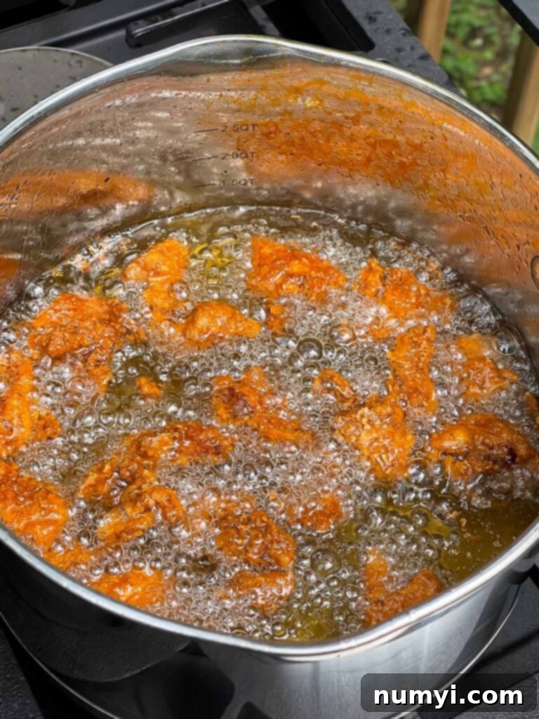 Bite sized chicken thigh pieces frying in oil.