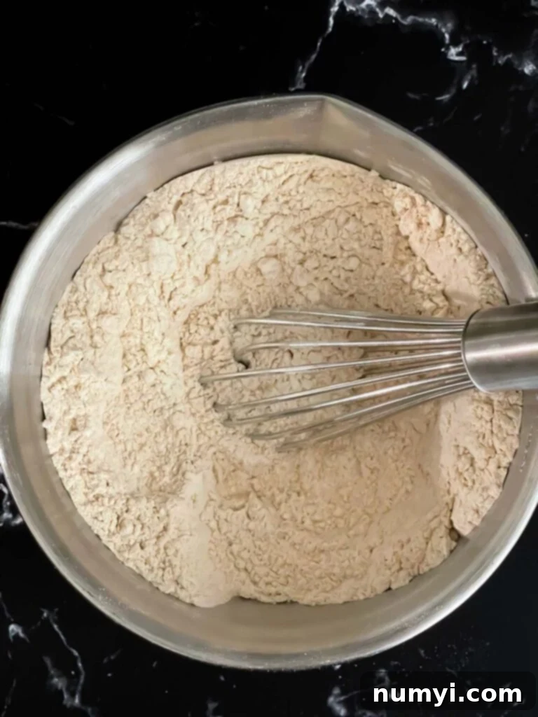 A bowl filled with carefully measured dry ingredients like flour, baking powder, salt, cinnamon, and nutmeg, ready to be whisked together for the muffin batter.