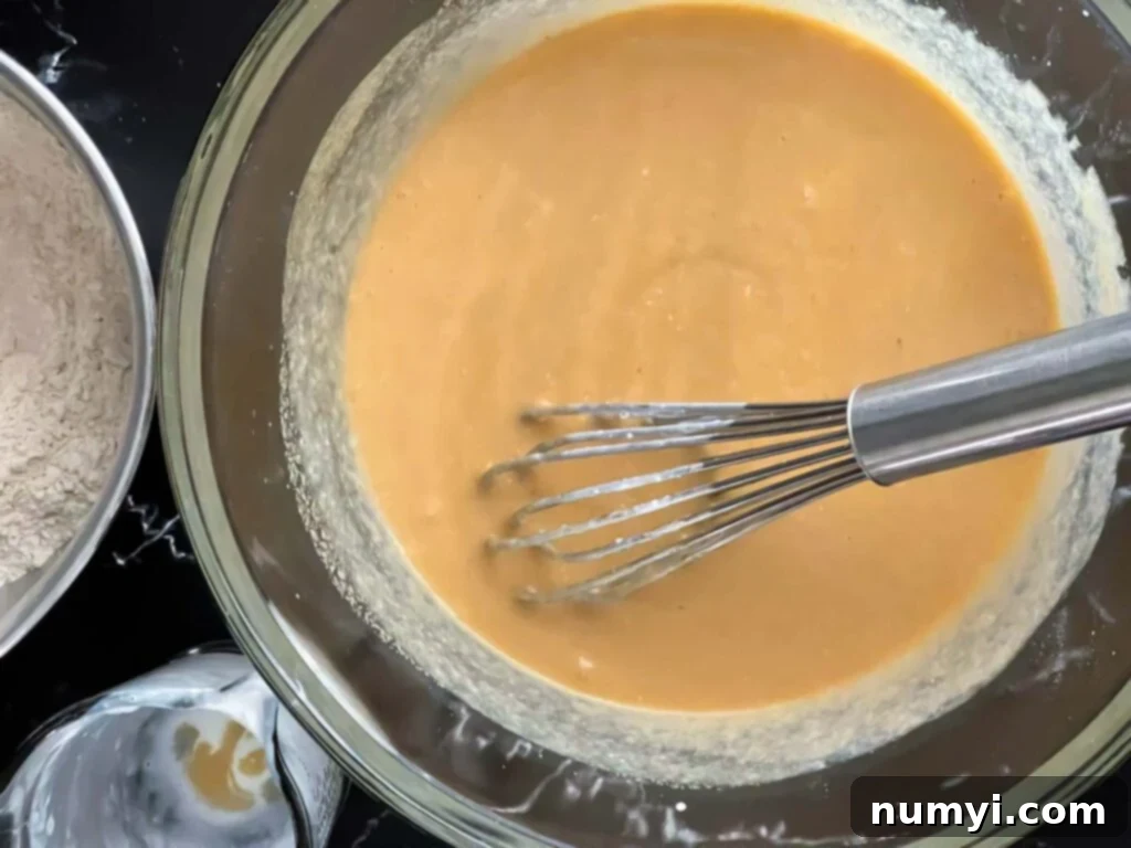 The combined wet ingredients, including whisked eggs and sugar, melted butter, buttermilk, and vanilla extract, thoroughly mixed in a large glass bowl until smooth.