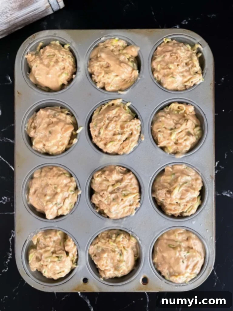 Unbaked zucchini muffin batter generously scooped into paper liners within a muffin tin, displaying its readiness for the oven.