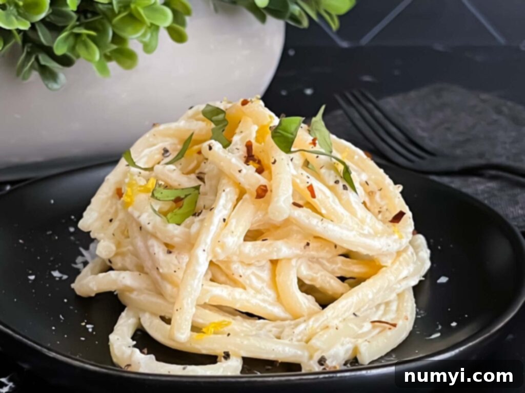 Lemon Ricotta pasta, topped with black pepper and basil, on a dark plate.