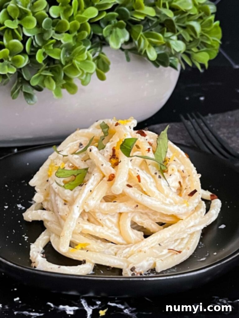 Lemon Ricotta Pasta, topped with black pepper and basil, on a dark plate.