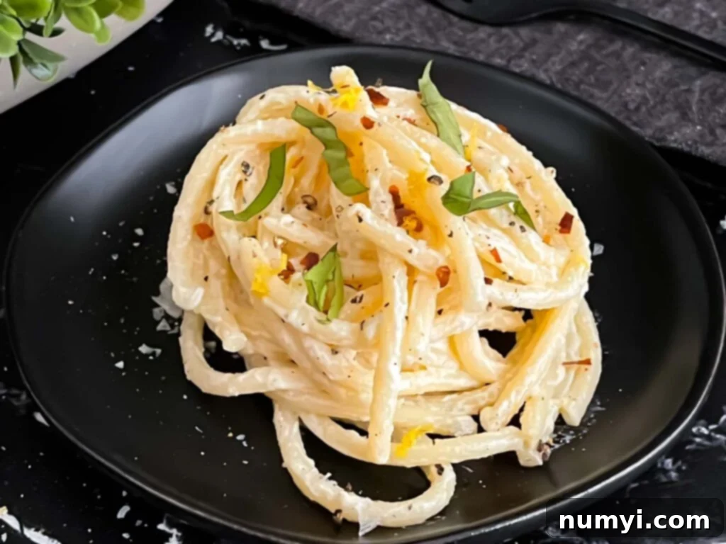 Lemon Ricotta pasta, topped with black pepper and basil, on a dark plate.