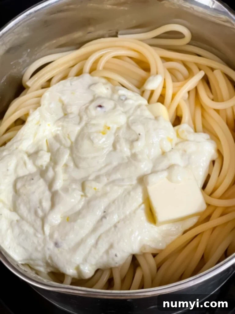 A lemon ricotta sauce being added to pasta in a cooking pot.