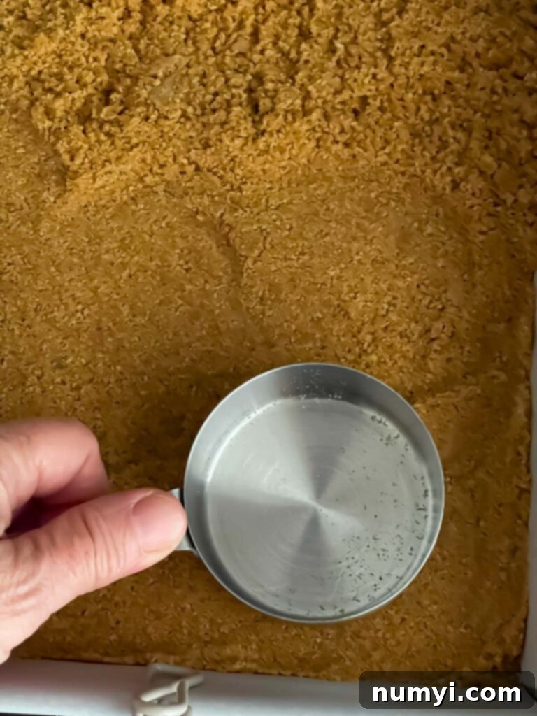 Smores Bars 5 Firmly pressing graham cracker crust into a parchment-lined baking pan.