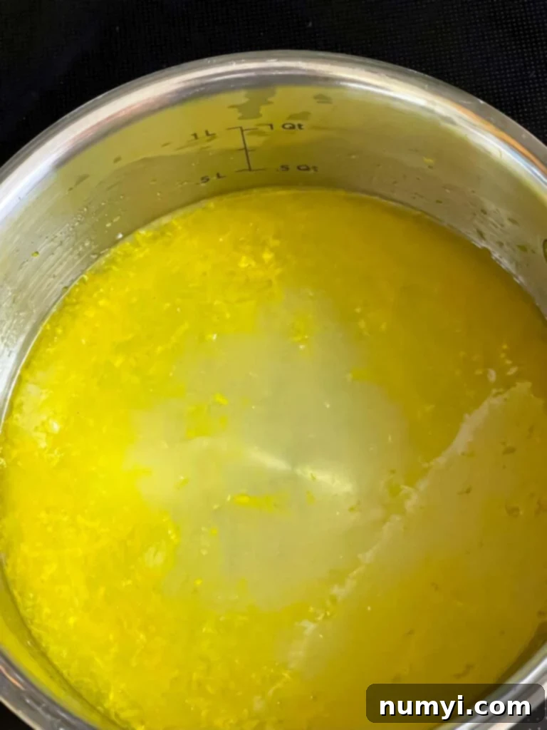 Limoncello syrup being prepared in a small metal saucepan, showing lemon zest and juice.