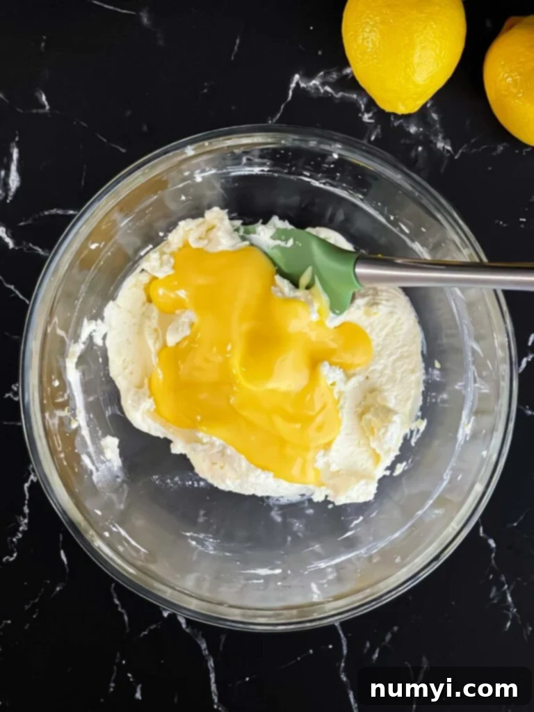 Lemon curd being gently folded into the limoncello mascarpone mixture in a glass bowl.