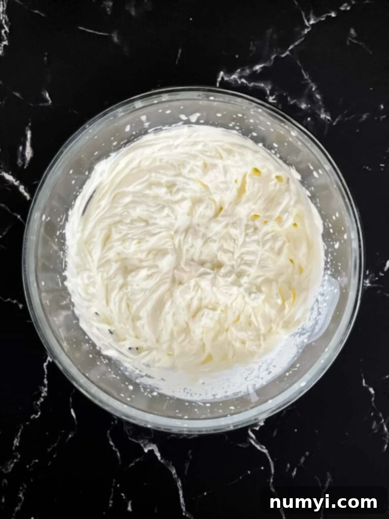 Heavy cream whipped to stiff peaks in a glass mixing bowl, ready to be incorporated into the mascarpone.
