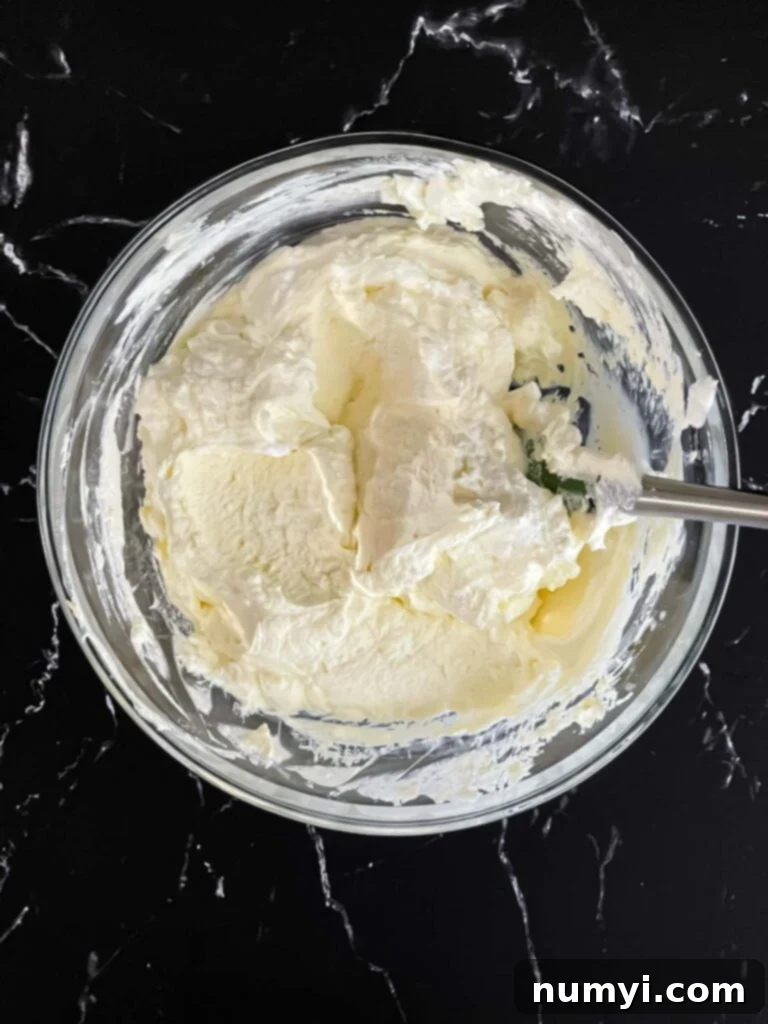 Lemon curd gently folded into the light and fluffy whipped cream in a glass mixing bowl.
