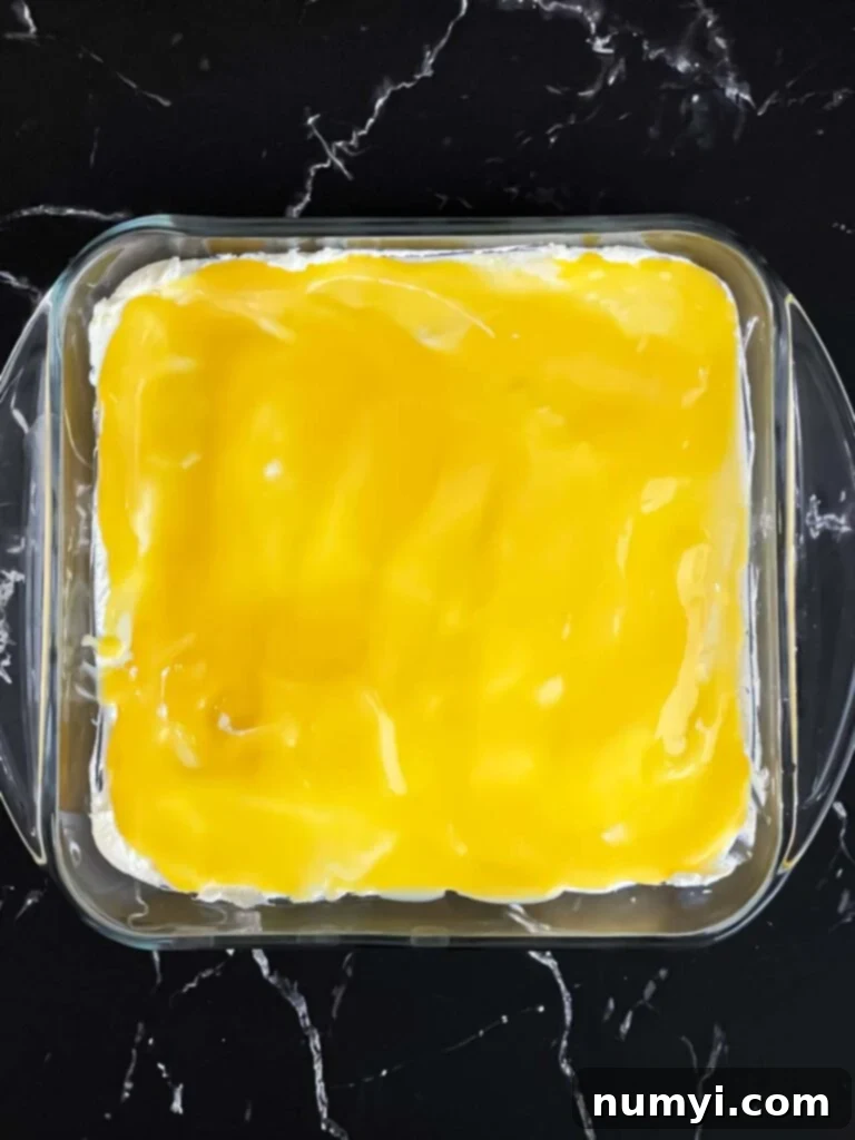 A layer of bright lemon curd spread over the creamy limoncello mascarpone in a glass baking dish.