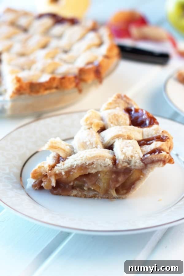 A single slice of luscious caramel apple pie on a white plate, with the whole pie blurred in the background, showcasing its rich filling.