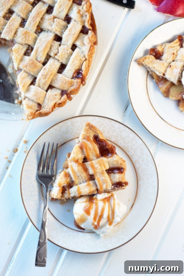 An overhead view of two slices of caramel apple pie on a plate, garnished with a scoop of vanilla ice cream and caramel drizzle, with the rest of the pie in the background.