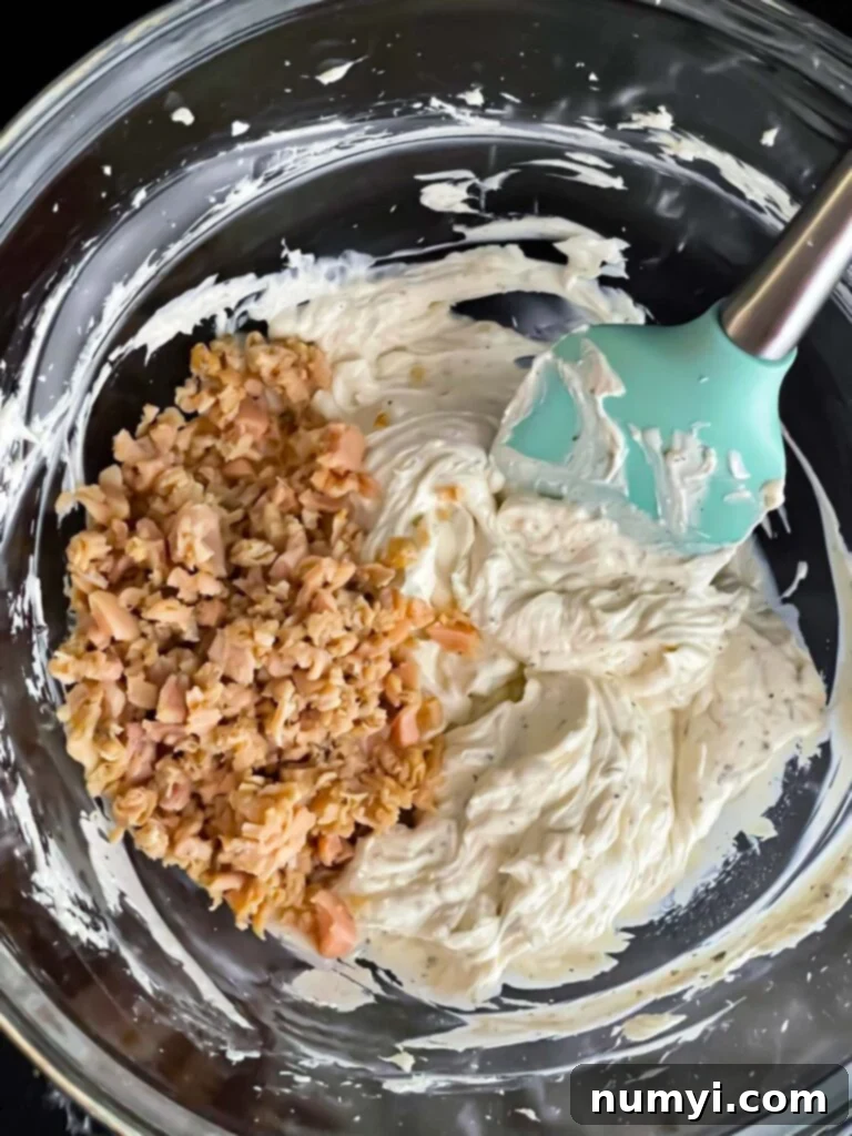 Clam dip ingredients in a glass mixing bowl with the minced clams on top.