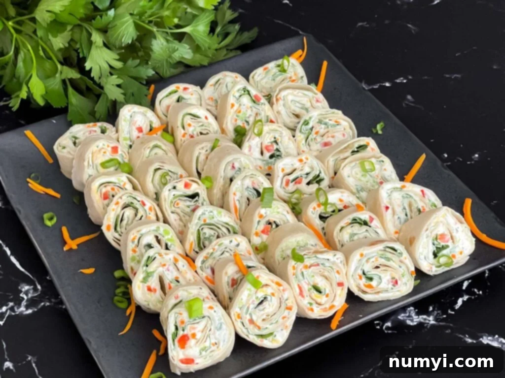 Veggie Tortilla Pinwheels 2 Vibrant veggie tortilla roll ups arranged neatly on a dark square plate, garnished with fresh diced green onions and shredded carrots, ready to be served.