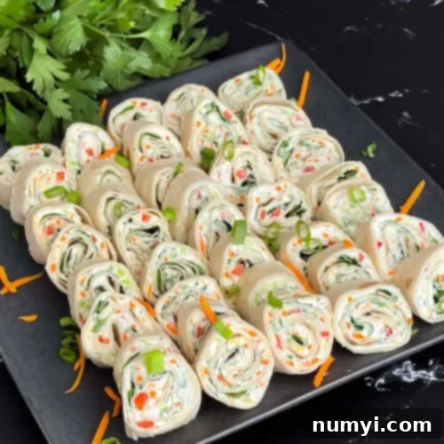 Veggie Tortilla Pinwheels 11 Veggie tortilla roll ups lined up on a square dark plate garnished with diced green onions and shredded carrots.