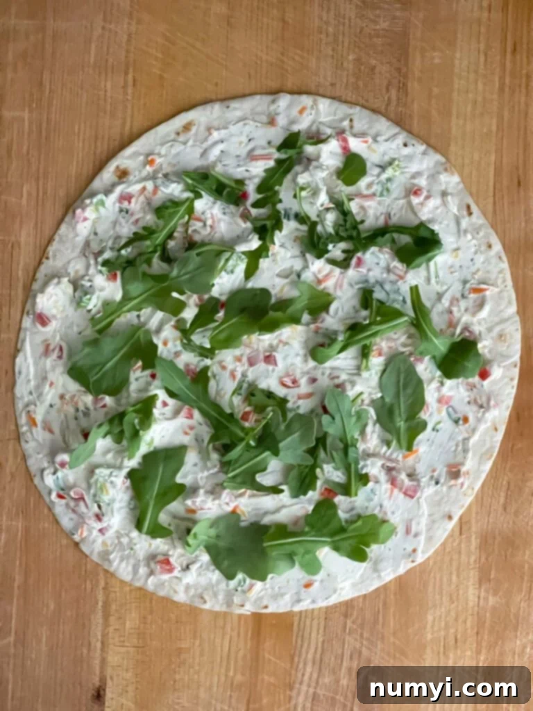 Veggie Tortilla Pinwheels 6 One tortilla on a wooden cutting board layered with the cream cheese mixture and baby arugula.