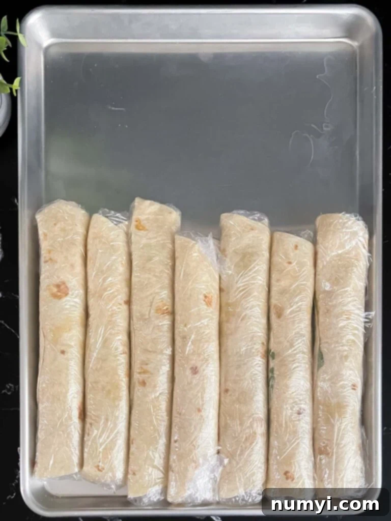 Veggie Tortilla Pinwheels 8 Veggie tortilla roll ups wrapped individually in plastic wrap, lined up on a baking sheet.