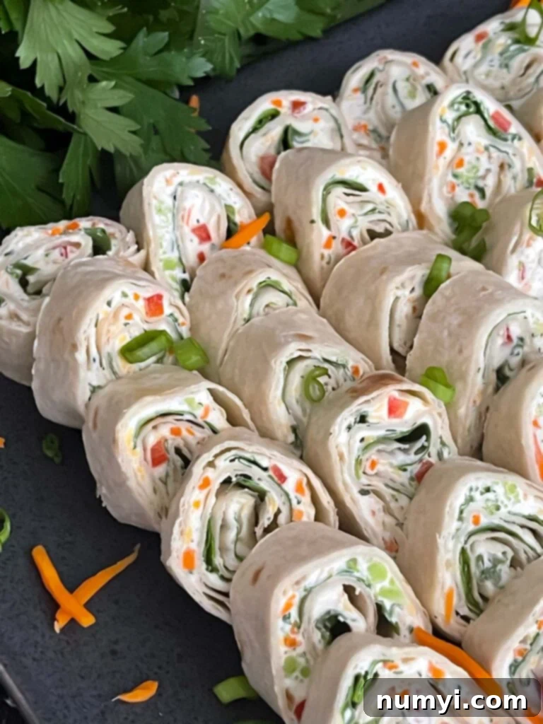 Veggie Tortilla Pinwheels 10 Veggie tortilla roll ups lined up on a square dark plate garnished with diced green onions and shredded carrots.