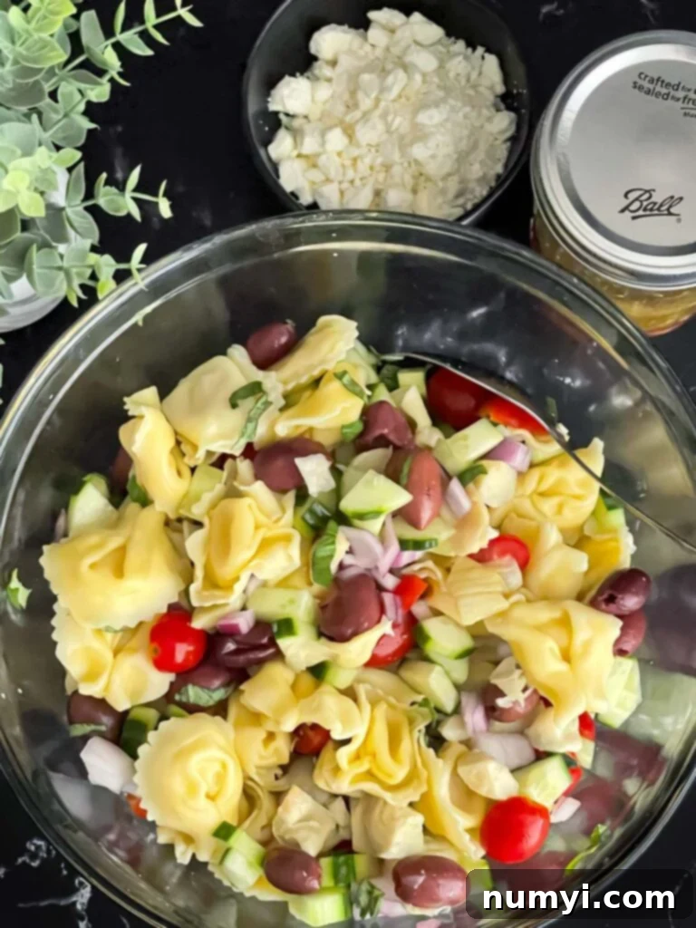 Vibrant Greek Tortellini Pasta Salad 7 A glass mixing bowl filled with colorful tortellini, chopped vegetables, and olives, gently tossed together for a Greek pasta salad.