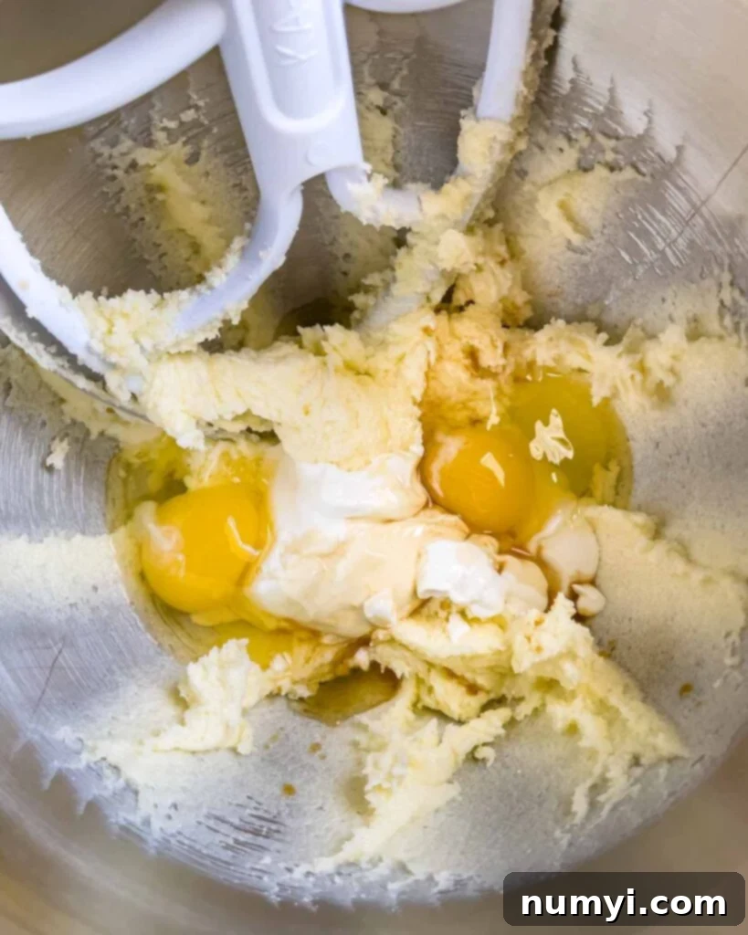 Eggs, sour cream, and vanilla extract added to the creamed butter in a metal mixing bowl.