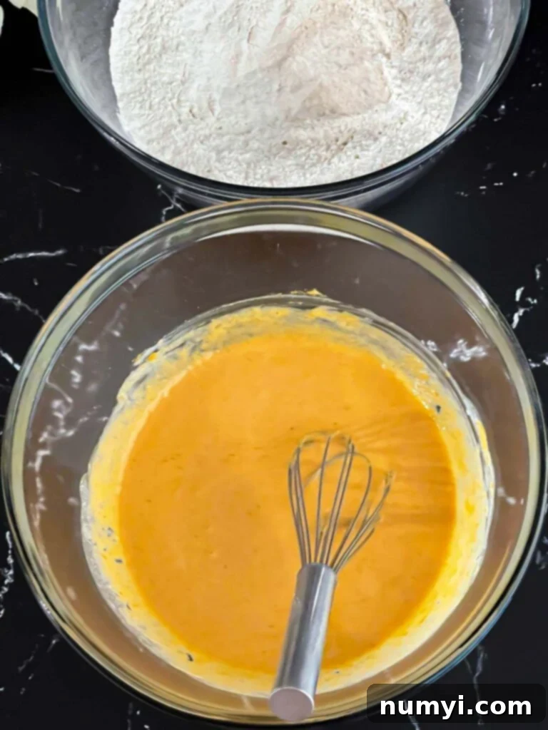 Pumpkin scones dry ingredients in a dark bowl and wet ingredients in a glass mixing bowl on a dark surface.