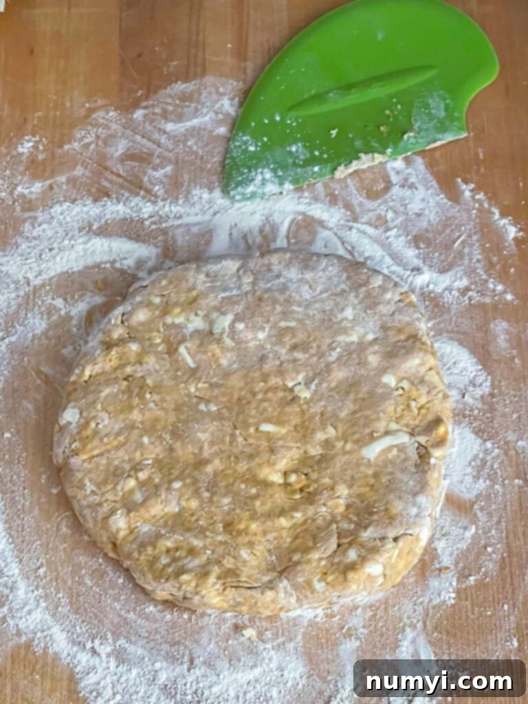 Pumpkin scone dough shaped into a 1-inch thick circle on a floured wooden board.