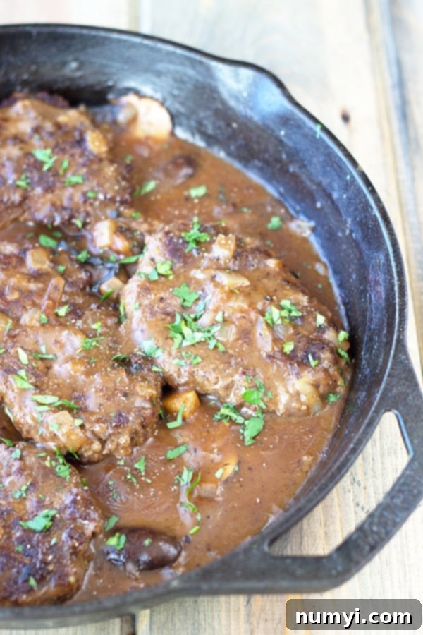 salisbury steaks in an onion gravy sauce with garnish in a cast iron skillet