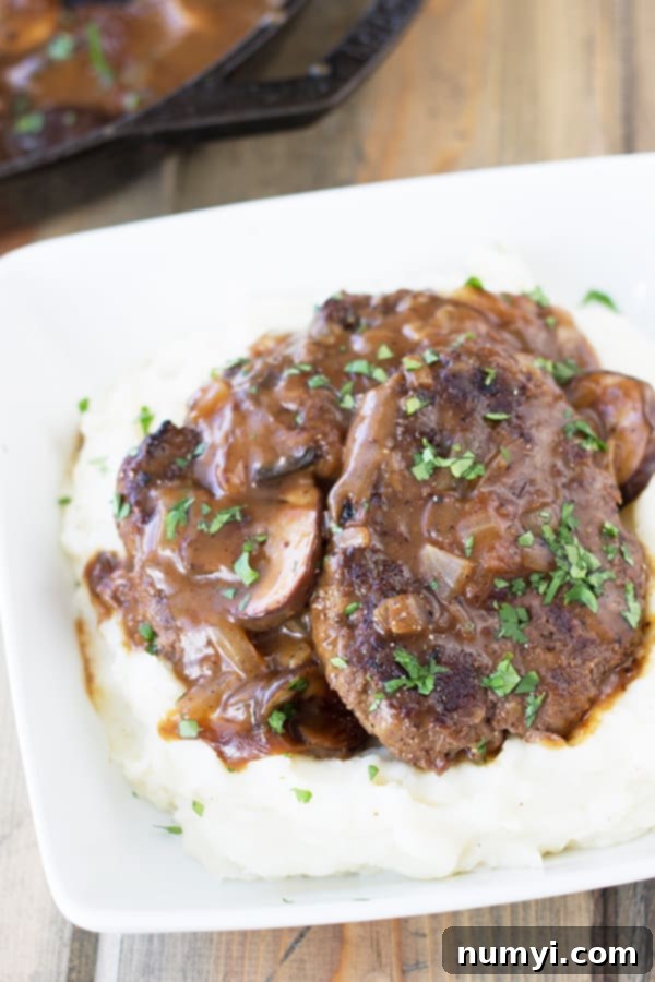 homemade Salisbury Steak with Mushrooms served over creamy mashed potatoes in a white dish