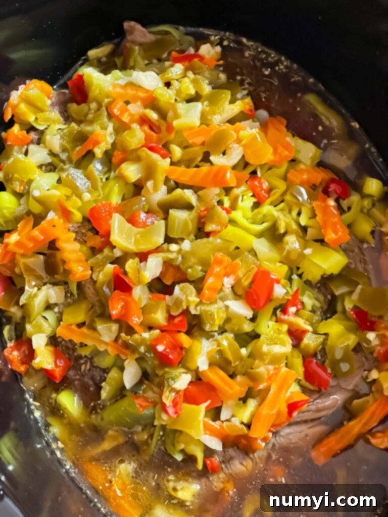 Melt-in-Your-Mouth Slow Cooker Italian Beef Sandwiches 7 Pepperoncini and giardiniera spread over the seasoned roast in the slow cooker, ready for cooking.