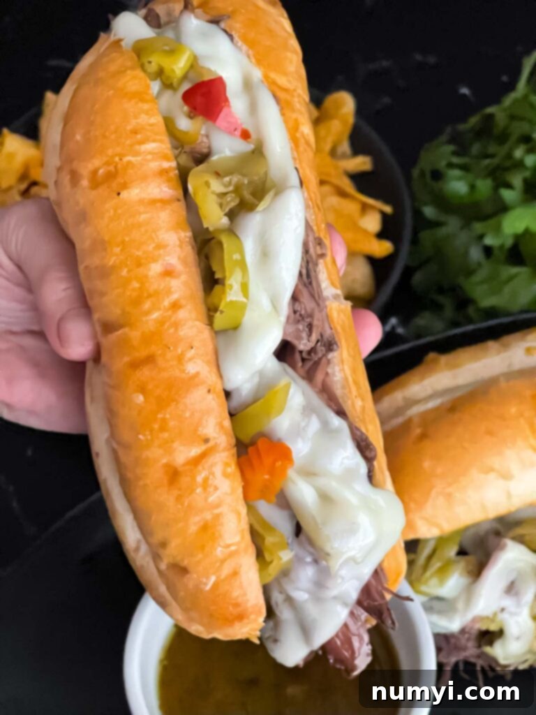Melt-in-Your-Mouth Slow Cooker Italian Beef Sandwiches 10 A completed Italian beef sandwich with melted cheese, peppers, and giardiniera, served with a side of au jus.
