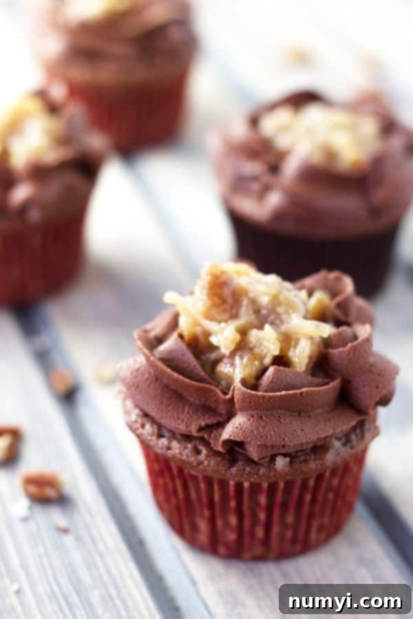 German Chocolate Cupcakes 5 One German chocolate cupcake in focus with three others out of focus in the background, highlighting its delicious appearance.