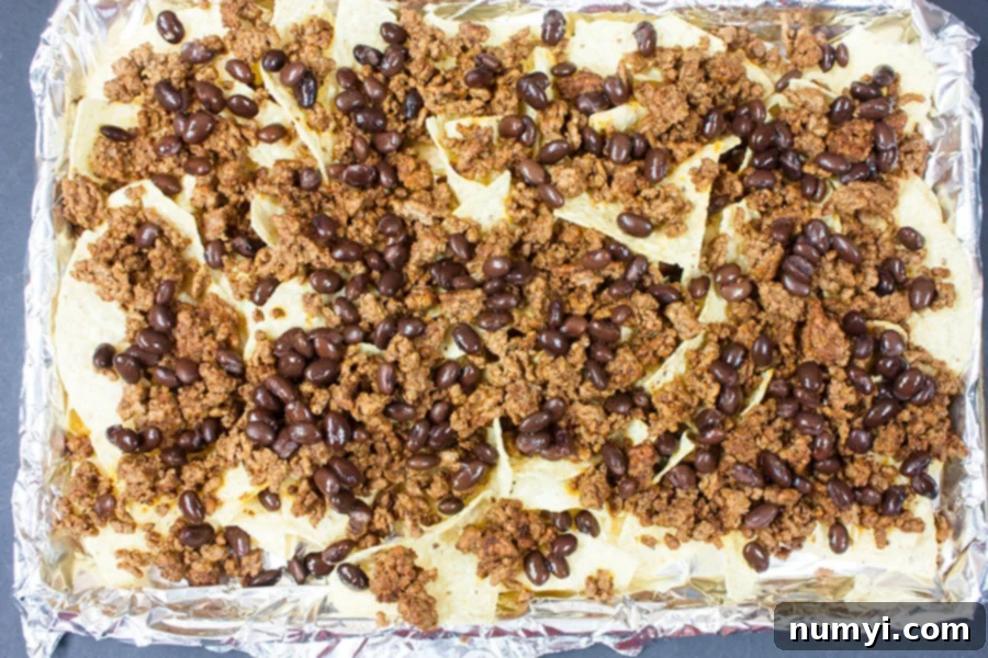 Tortilla chips, ground beef, and black beans on a foil-lined baking sheet before baking
