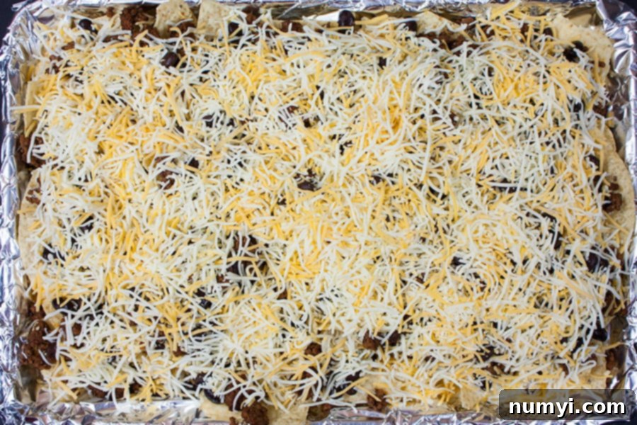 Tortilla chips, ground beef, black beans, and shredded cheese layered on a foil lined baking sheet
