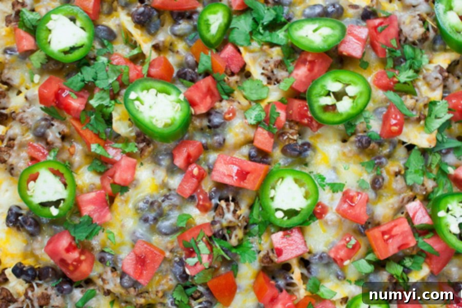 Sheet Pan Beef Nachos topped with a variety of fresh ingredients including tomatoes, green onions, jalapenos, and lime wedges.